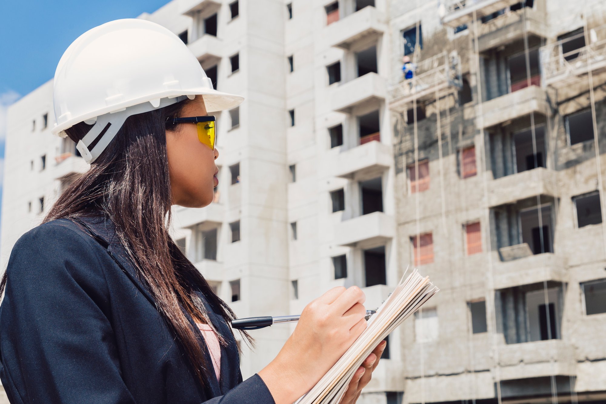 african-american-lady-safety-helmet-writing-notepad-near-building-construction